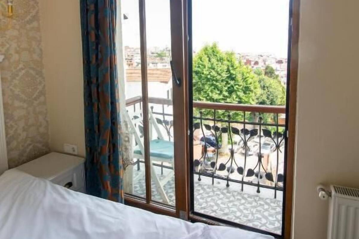 A hotel room with a bed, a window with a view of a balcony and outside buildings, and a radiator.