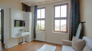 A room with a white sofa, a small white table, a TV mounted on the wall, and two windows with curtains. - IQ Hotel Galatasaray (Istanbul)