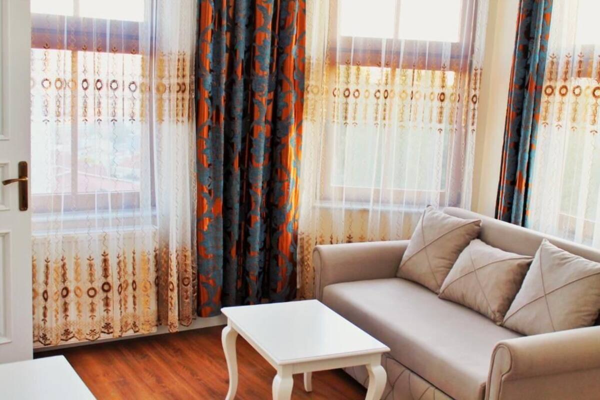 A room with a beige sofa, a small white table, and patterned curtains.