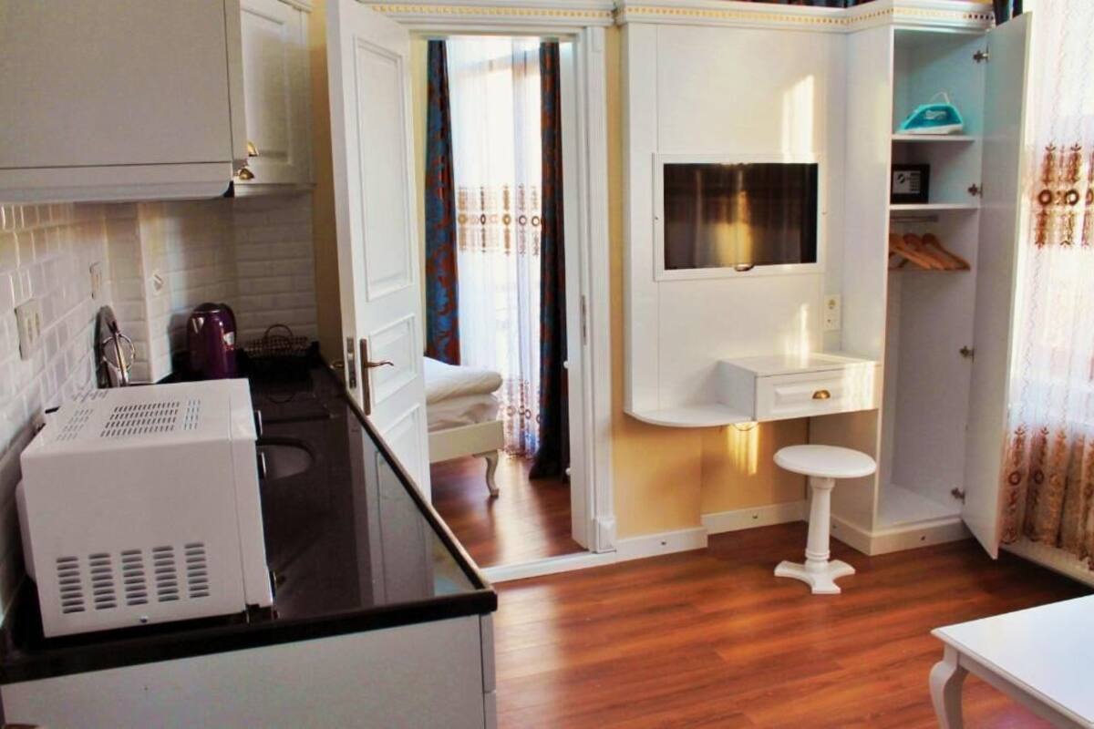 A compact kitchen with a black countertop, a white sink, and a small stool.