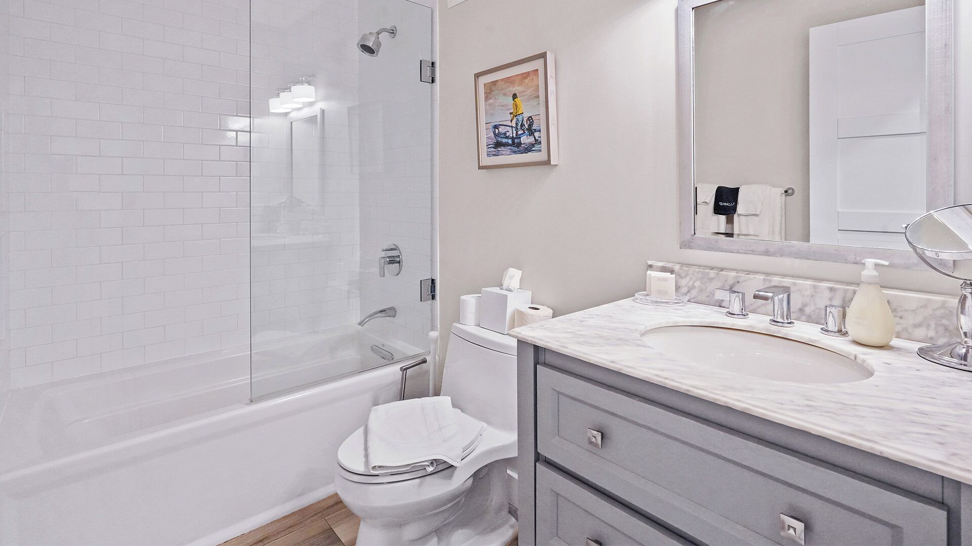 Une salle de bain moderne avec une douche à parois de verre, des toilettes blanches, un lavabo en marbre et une œuvre d’art encadrée accrochée au mur.