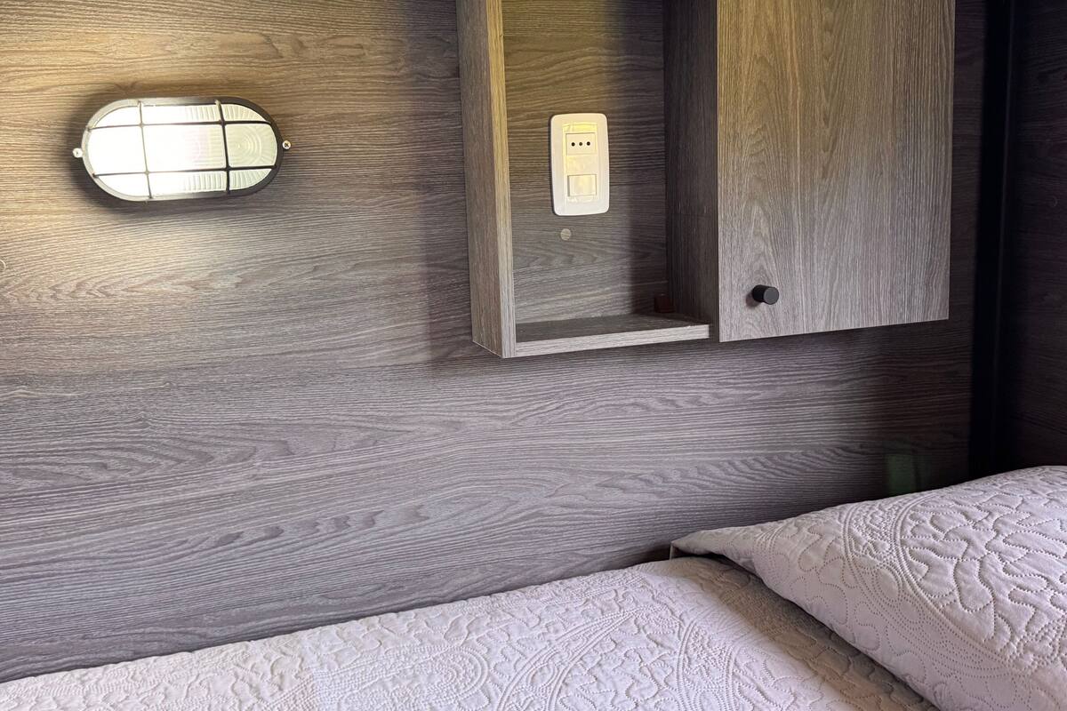 A compact room with a bed, a built-in cabinet with a power outlet, and a small window.