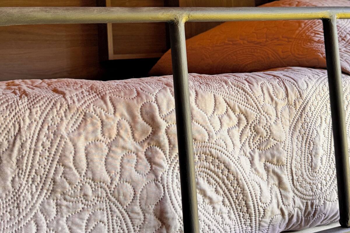 A bunk bed with a patterned quilt, a wooden headboard, and a small bedside table with a light switch.