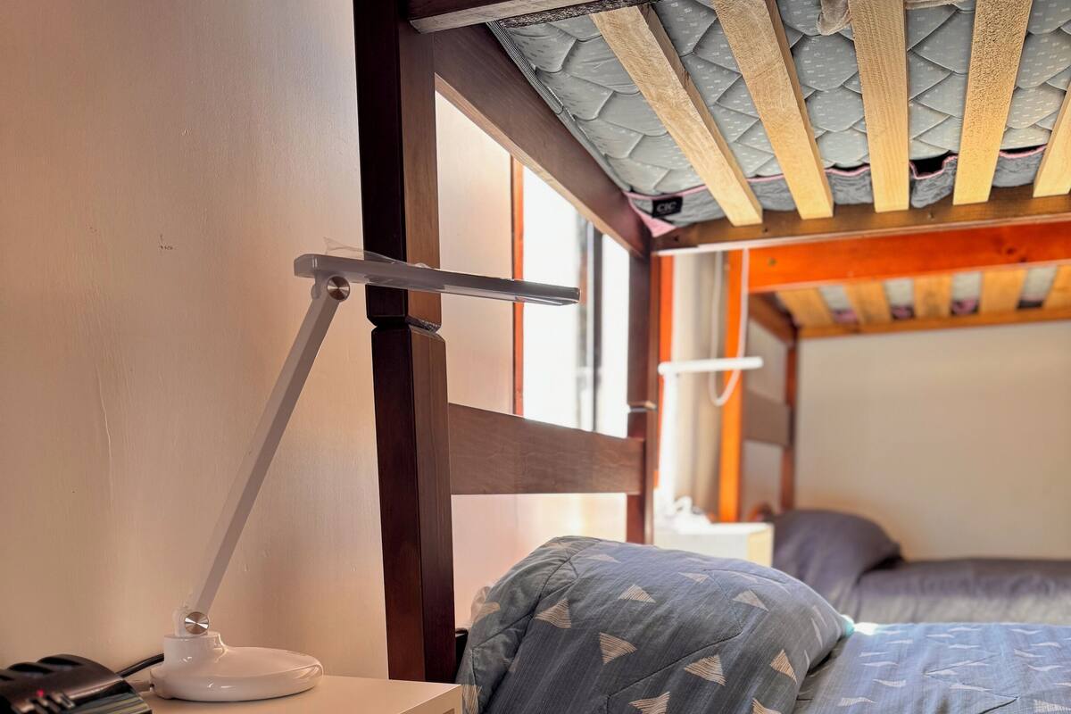A bedroom with a wooden bed, a desk with a lamp, and a window with a view.