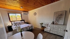 Une chambre à coucher avec un lit, une table de chevet et une commode. Il y a une fenêtre qui donne sur un paysage verdoyant.