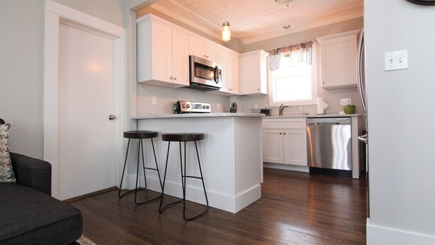 A modern kitchen with white cabinets, a built-in microwave, and a dishwasher. There are two bar stools near the kitchen counter. - 9 Lake Street  (Wolfeboro)