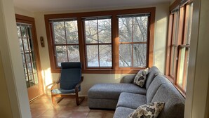 A living room with a sectional sofa, a rocking chair, and large windows with a view of trees.