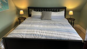 A bedroom with a bed, two bedside tables, two lamps, and a painting on the wall.