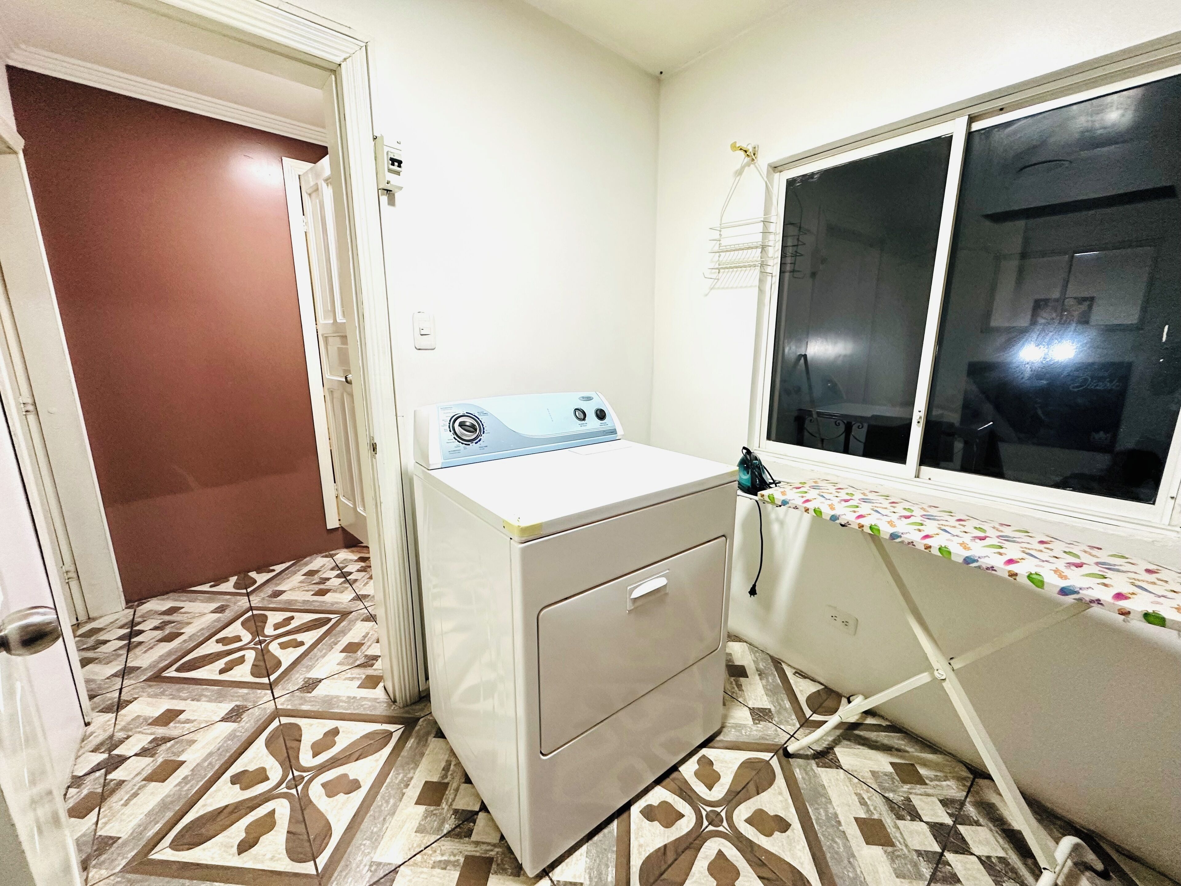 A laundry room with a washing machine, a drying rack, and patterned floor tiles.