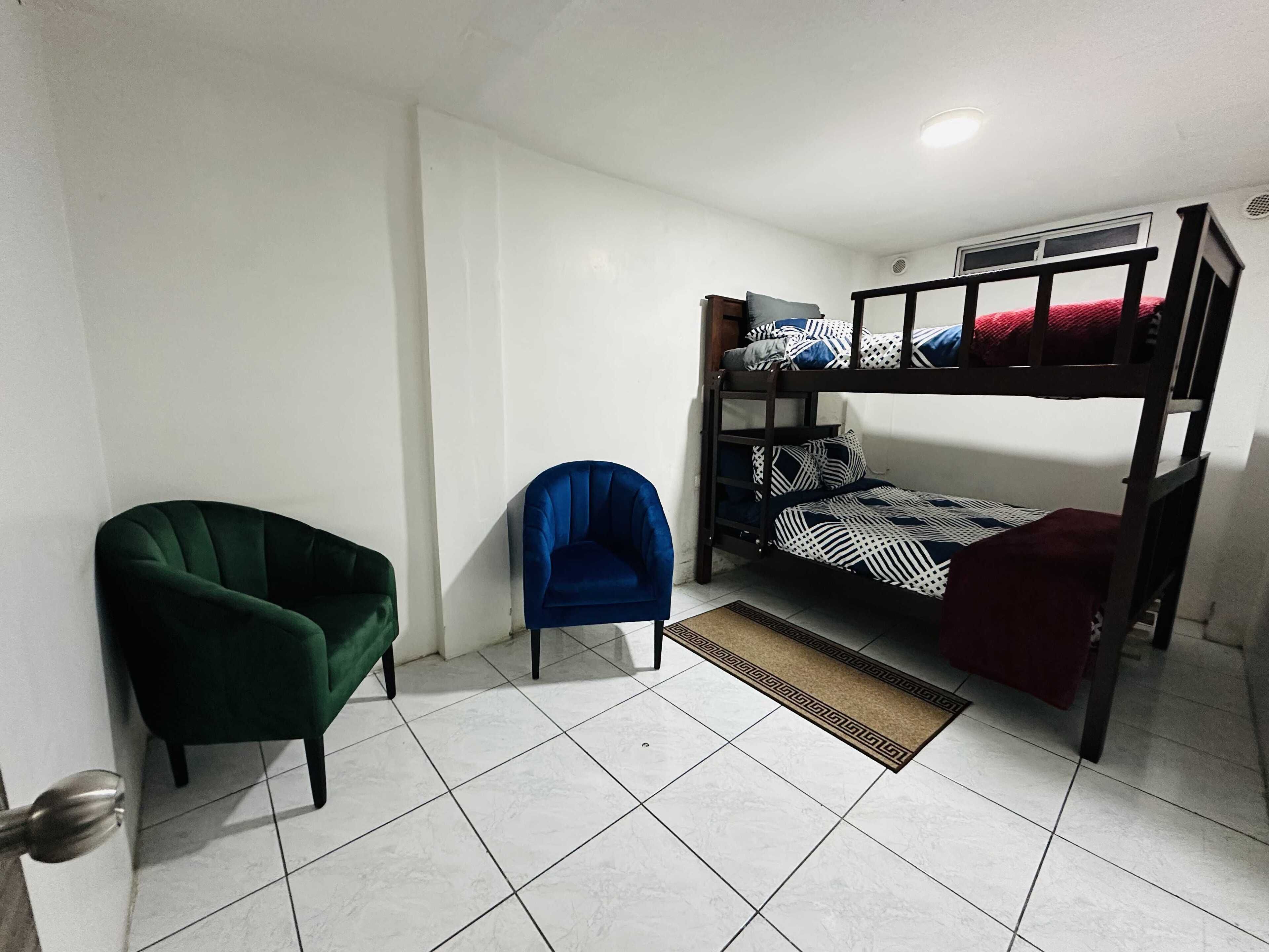 Une petite pièce, de taille modeste, comprenant un lit superposé, un fauteuil vert et une chaise bleue.