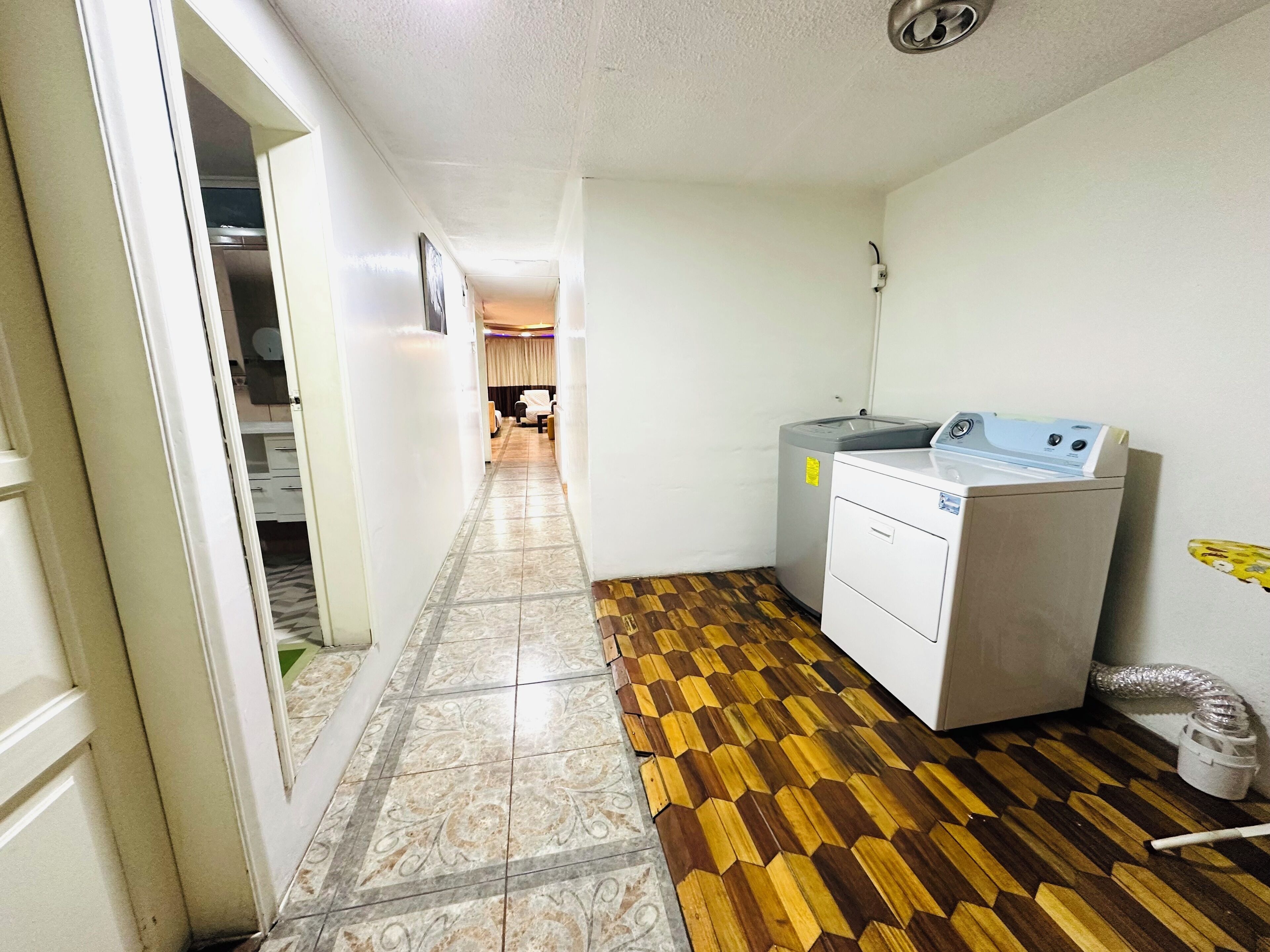 A hallway with a patterned floor leading to a room with a washing machine and a radiator.