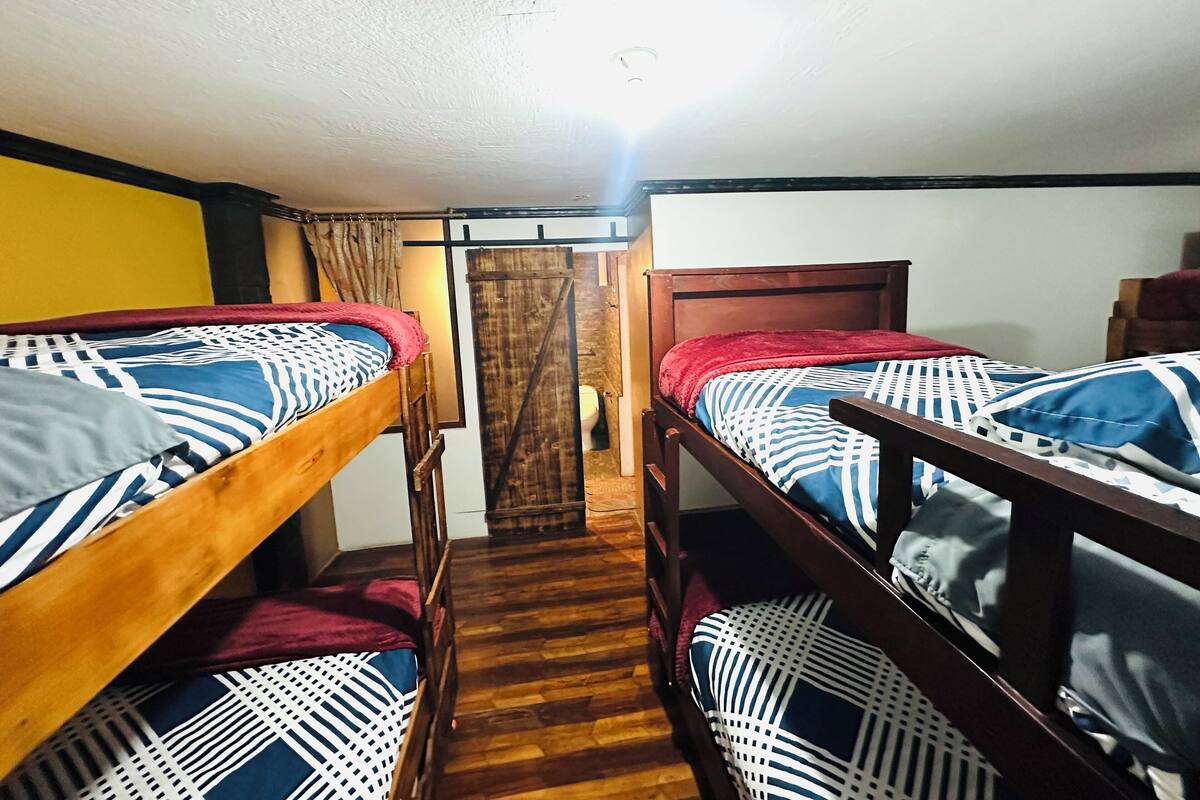 Una habitación con dos literas, suelo de madera, una puerta de madera y una cortina.