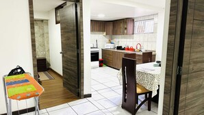 Una cocina moderna con armarios de madera, un comedor con mesa y sillas, y un taburete pequeño con un felpudo colorido.