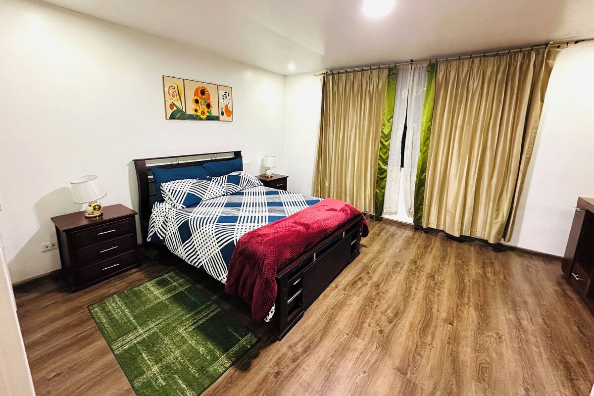 Un dormitorio con cama, mesita de noche, lámpara, alfombra verde y un cuadro en la pared.