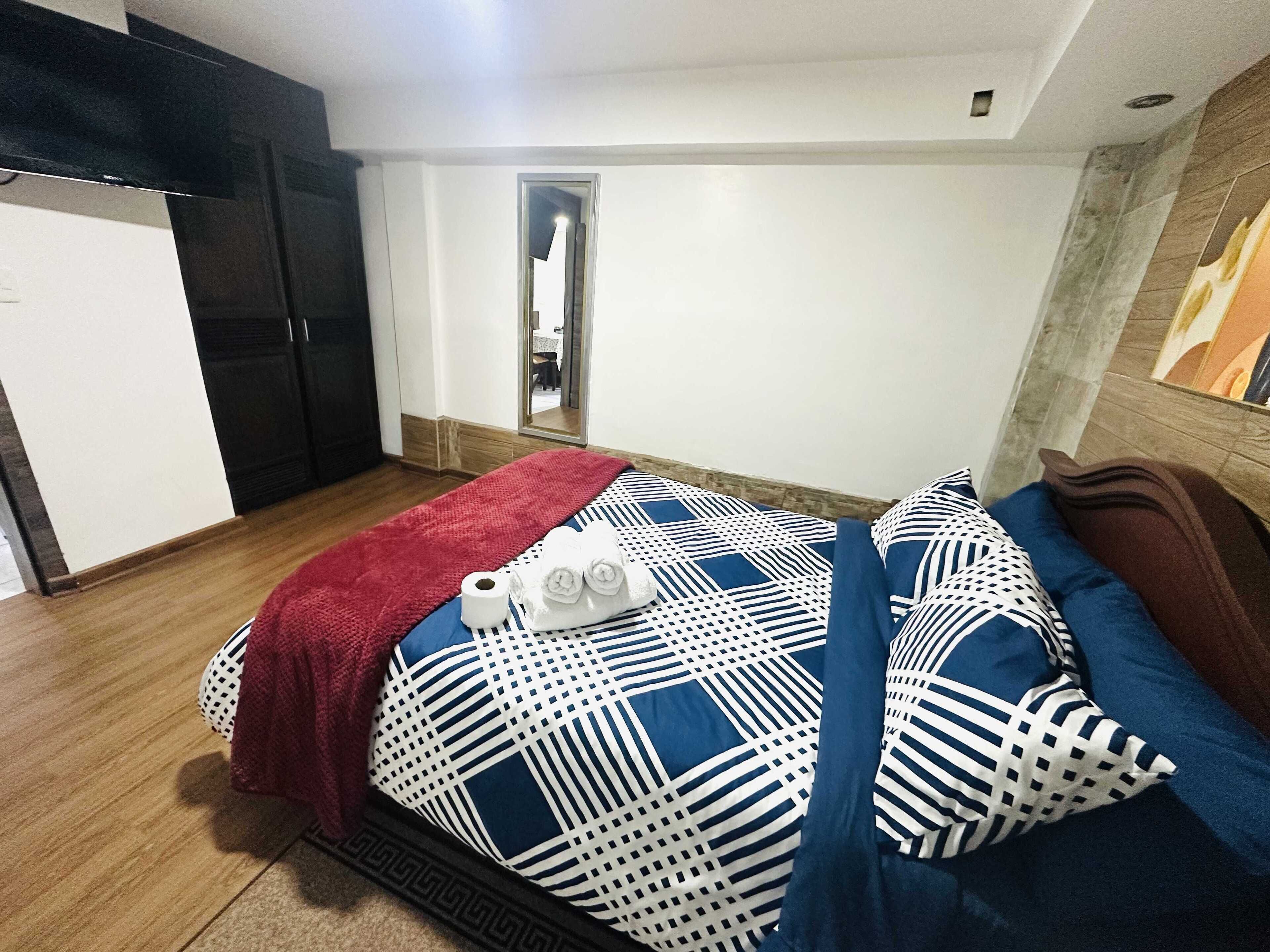 Una habitación de hotel con una cama, un plaid rojo y toallas.
