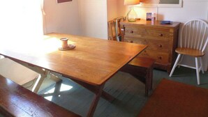 Una mesa de madera para comer con una vela, un aparador con cajones, una silla y una lámpara.