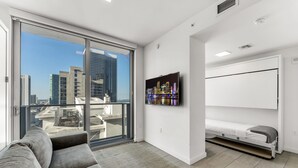 A modern living room with a gray sofa, a wall-mounted TV, and a built-in bed unit. - Stylish Studio + Den Across from Bayside Miami! (Miami)