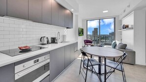 A modern kitchen with grey cabinets, white tiles, and a large window offering a city view. - Stylish Studio + Den Across from Bayside Miami! (Miami)