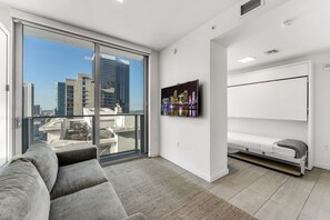A modern living room with a sofa, a mounted TV, and a bed with a mattress on the floor.