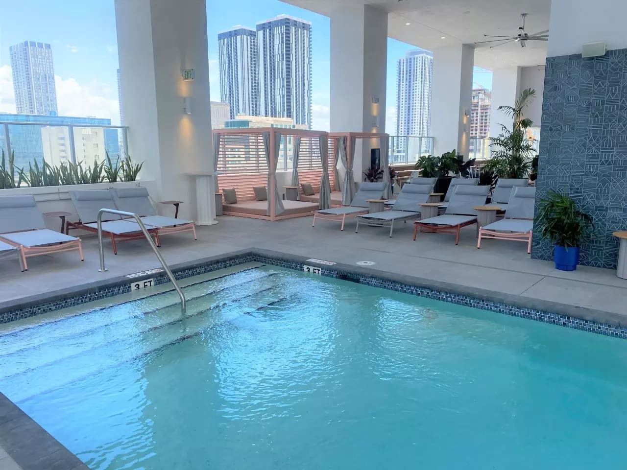 An indoor pool with lounge chairs and a view of tall buildings.