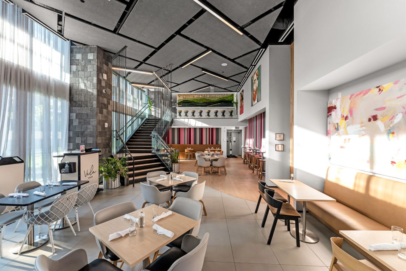 A modern restaurant with a staircase, dining tables, chairs, and a large window.
