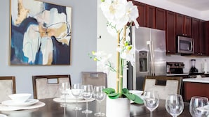 A dining table set with white plates, bowls, and wine glasses, surrounded by chairs. A potted orchid is placed in the center. - Amazing 8BR Family Villa at Veranda Palms ● Private Pool/BBQ/More! (Kissimmee)