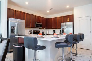 Une cuisine moderne dotée d’appareils électroménagers en acier inoxydable, de meubles en bois et d’un îlot central avec des tabourets de bar.