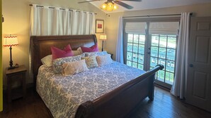 A bedroom with a bed, a ceiling fan, a nightstand, a lamp, and a view through a window. - 2-Br Country Cottage on rolling hills of Burton, 15 min from Round Top! (Burton)