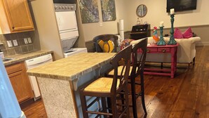 A kitchen with wooden cabinets, a built-in dishwasher, a dining area with a wooden table and chairs, and a pink side table with candles. - 2-Br Country Cottage on rolling hills of Burton, 15 min from Round Top! (Burton)