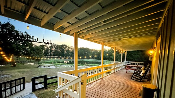 A covered outdoor deck with a wooden floor, white railings, and string lights. - 2-Br Country Cottage on rolling hills of Burton, 15 min from Round Top! (Burton)