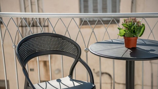 Une chaise en métal noir et une petite table ronde avec un pot de plante sur un balcon.