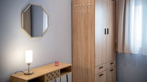 Une chambre avec une armoire en bois, un miroir, une table de chevet avec une lampe et une fenêtre avec des rideaux.