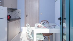 A compact kitchen with a refrigerator, a kettle, and a dining table with chairs. - M City Apartments | Garden 1 | 100m from the beach (Chania)