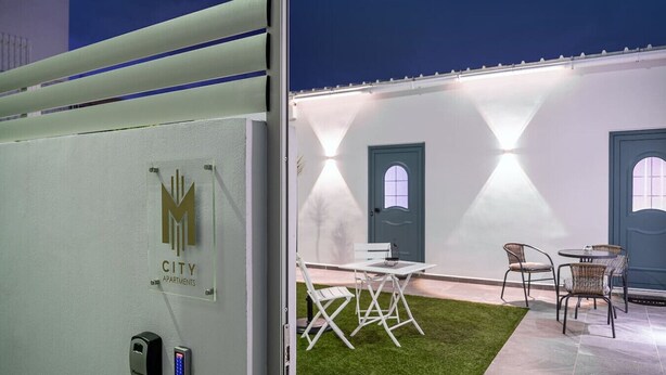 A modern apartment complex with a well-lit entrance, outdoor seating area, and a green lawn. - M City Apartments | Garden 1 | 100m from the beach (Chania)