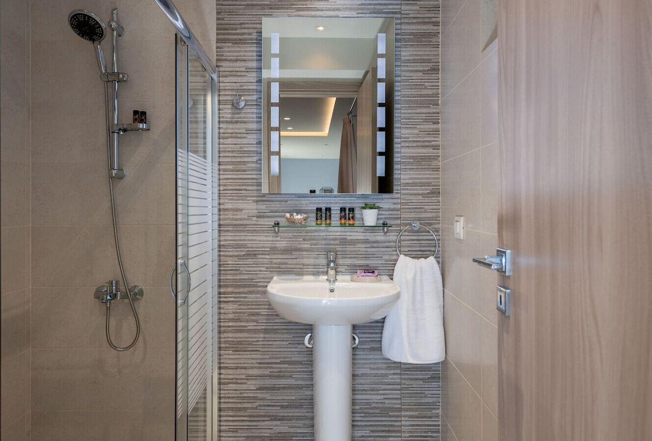 A modern bathroom with a glass shower enclosure, a pedestal sink, and a mirror above the sink.