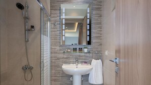 A modern bathroom with a glass shower enclosure, a pedestal sink, and a mirror above the sink. - M City Apartments | Garden 1 | 100m from the beach (Chania)