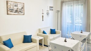 Una sala de estar con un sofá, dos sillones, una mesa de centro y una mesa de comedor con sillas. Hay un cuadro en la pared y un letrero que dice "Relax Beach".