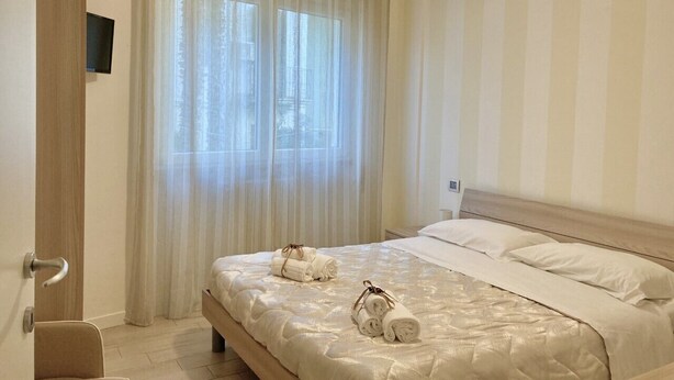 Una habitación de hotel con cama, cortinas, un accesorio de iluminación y una puerta de madera.