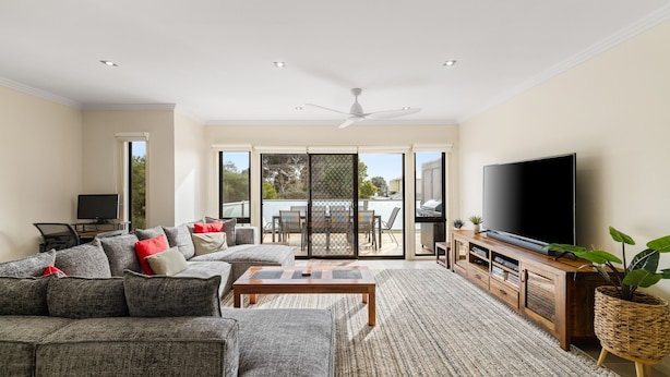 A living room with a sofa, coffee table, TV, and a sliding glass door leading to an outdoor area. - Brooklya by the Beach (Cowes)