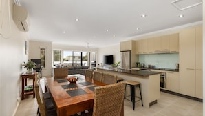 A modern kitchen with a central island, built-in appliances, and a dining area with a wooden table and wicker chairs. - Brooklya by the Beach (Cowes)