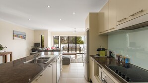 A modern kitchen with a central island, a dining area with a sofa and table, and a view of the outdoors. - Brooklya by the Beach (Cowes)