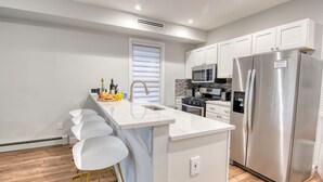 A modern kitchen with white cabinetry, stainless steel appliances, and a central island with bar stools.