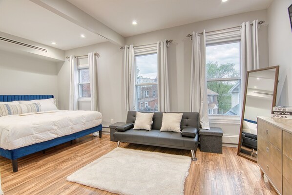 Un dormitorio con cama, sofá, espejo y vistas a edificios.