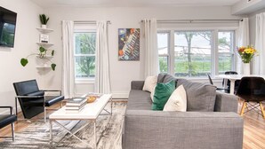 A modern living room with a grey sofa, a black chair, a white coffee table, and a bookshelf with plants.