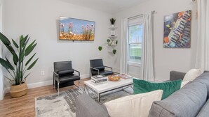 A modern living room with a sofa, two armchairs, a coffee table, and a large window with curtains.