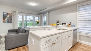 A modern kitchen with a central island, white cabinetry, and a grey sofa in the adjacent living area.
