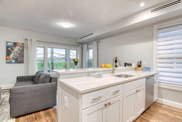Una cocina moderna con una isla central, muebles blancos y un sofá gris en la zona de estar contigua.