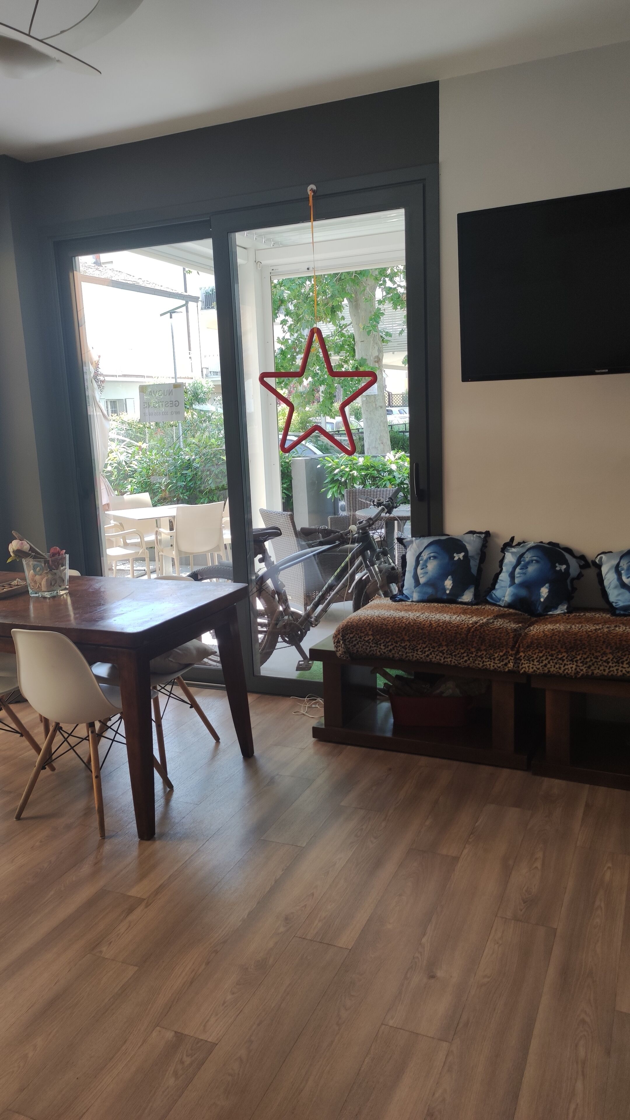 A modern living room with a wooden floor, a dining area with a table and chairs, a sofa with patterned cushions, and a large window with a star decoration.