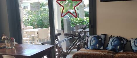 Una sala moderna con piso de madera, un comedor con mesa y sillas, un sofá con cojines estampados y un ventanal con decoración de estrellas.