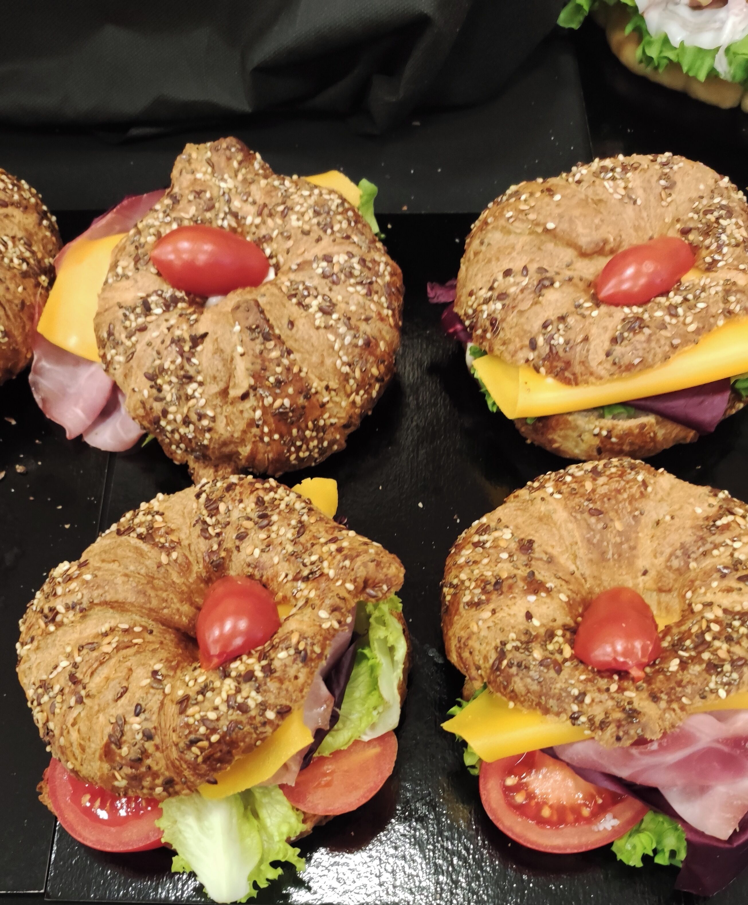 A tray of sandwiches with sesame seeds, cheese, lettuce, and tomatoes.